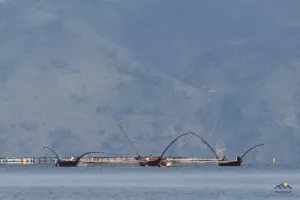 Fischerboote am See, dahinter schwimmende Fischfarmen